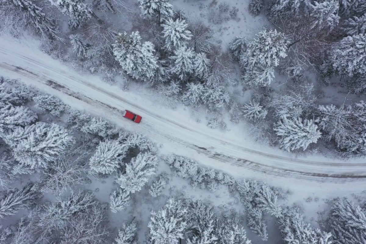 Load video: Red Car driving through snowing trees on a road